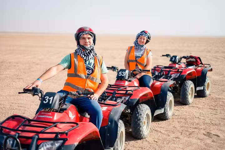 Riders on red ATVs in the Marsa Alam desert, part of quad safari with camel ride, Bedouin village and dinner