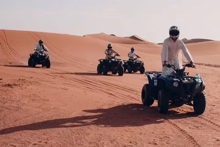 Group enjoying a thrilling self-drive quad bike ride across expansive desert dunes under a clear blue sky.