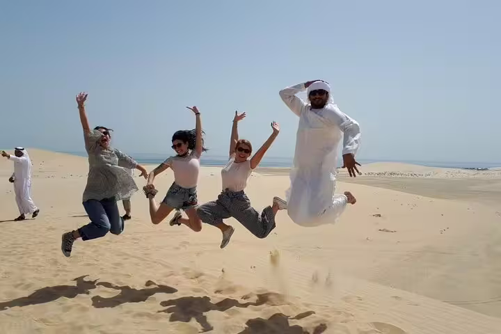 Group of excited tourists jumping joyfully on the sandy desert landscape under the bright sun.