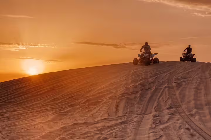 Two riders on quad bikes enjoying a thrilling desert dune adventure at sunset during a self-drive tour.