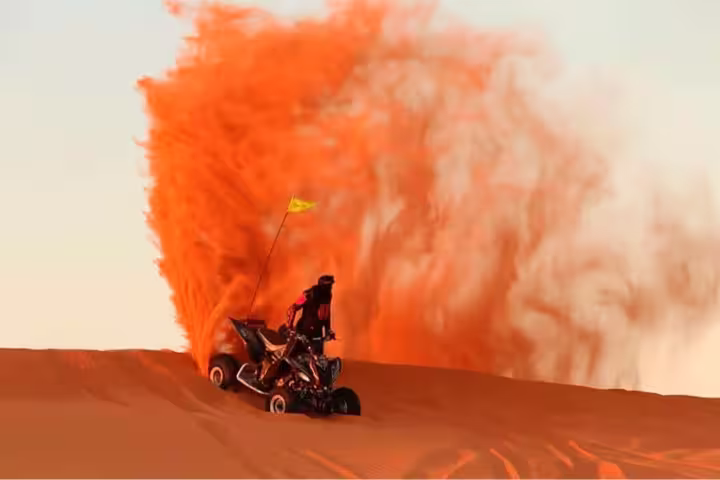 Thrilling desert adventure with a quad bike in Dubai, kicking up vibrant orange sand against a clear sky for an exhilarating ride.