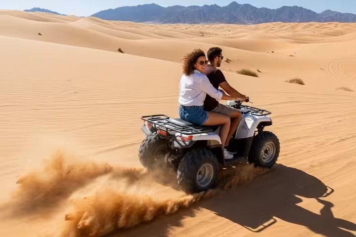 Rear view of quad biking in Sharm El Sheikh desert, couple carving dunes and kicking up sand trails