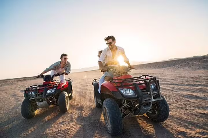 Two friends riding quad bikes across the Sharm El Sheikh desert with sun flare on a private ATV safari tour