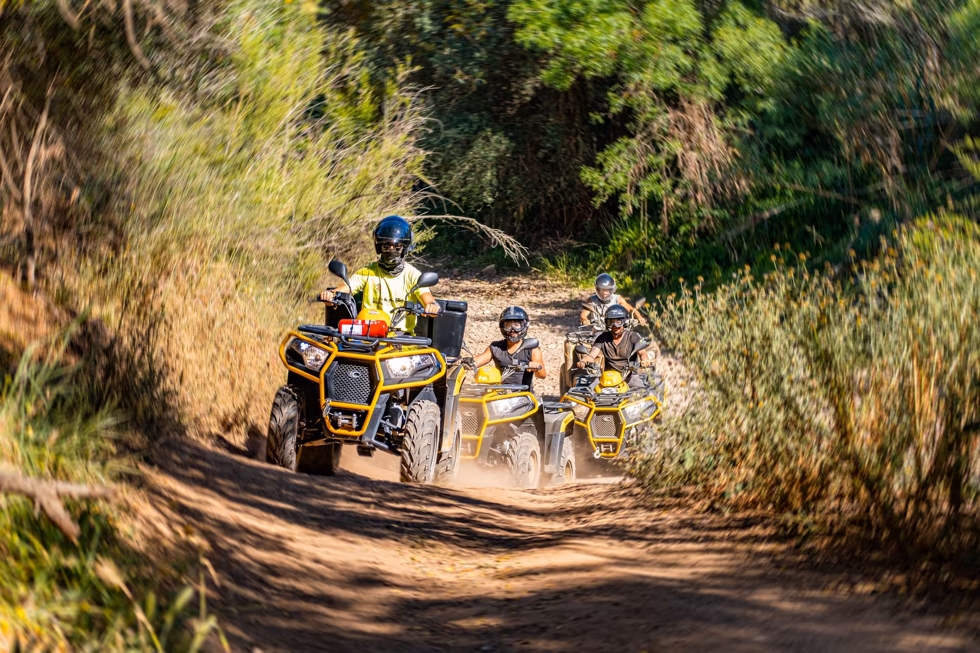 Guided quad bike tour group riding yellow ATVs along a dusty forest trail on an exciting off-road adventure