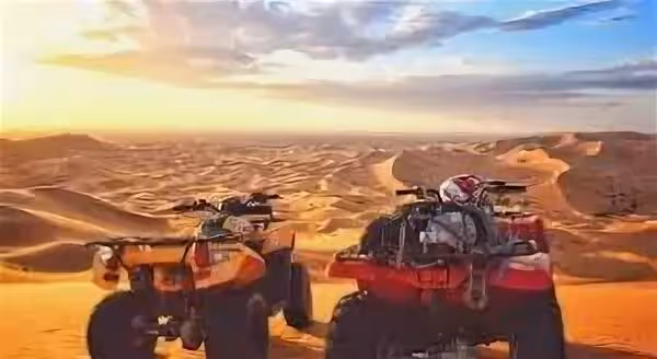 Two quad bikes parked on the golden sand dunes of Merzouga Erg Chebbi Desert at sunset, offering a stunning panoramic view.