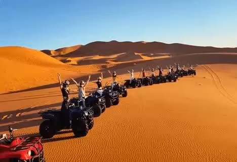 A group of adventurers on quad bikes lined up in the vast Merzouga Erg Chebbi Desert, celebrating under the sun.