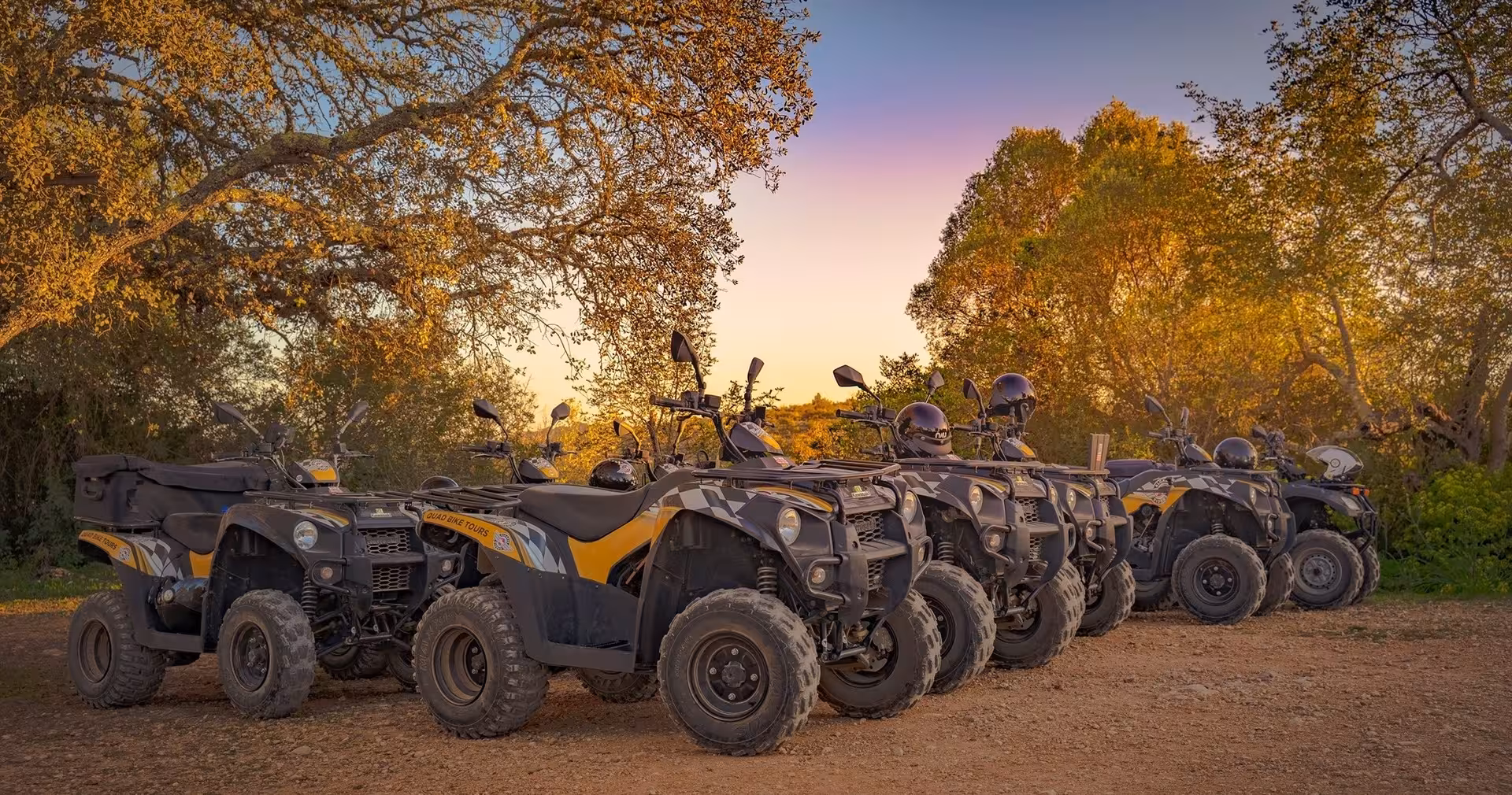 Row of parked quad bikes ready for an off-road tour at golden hour, surrounded by autumn trees and rural landscape