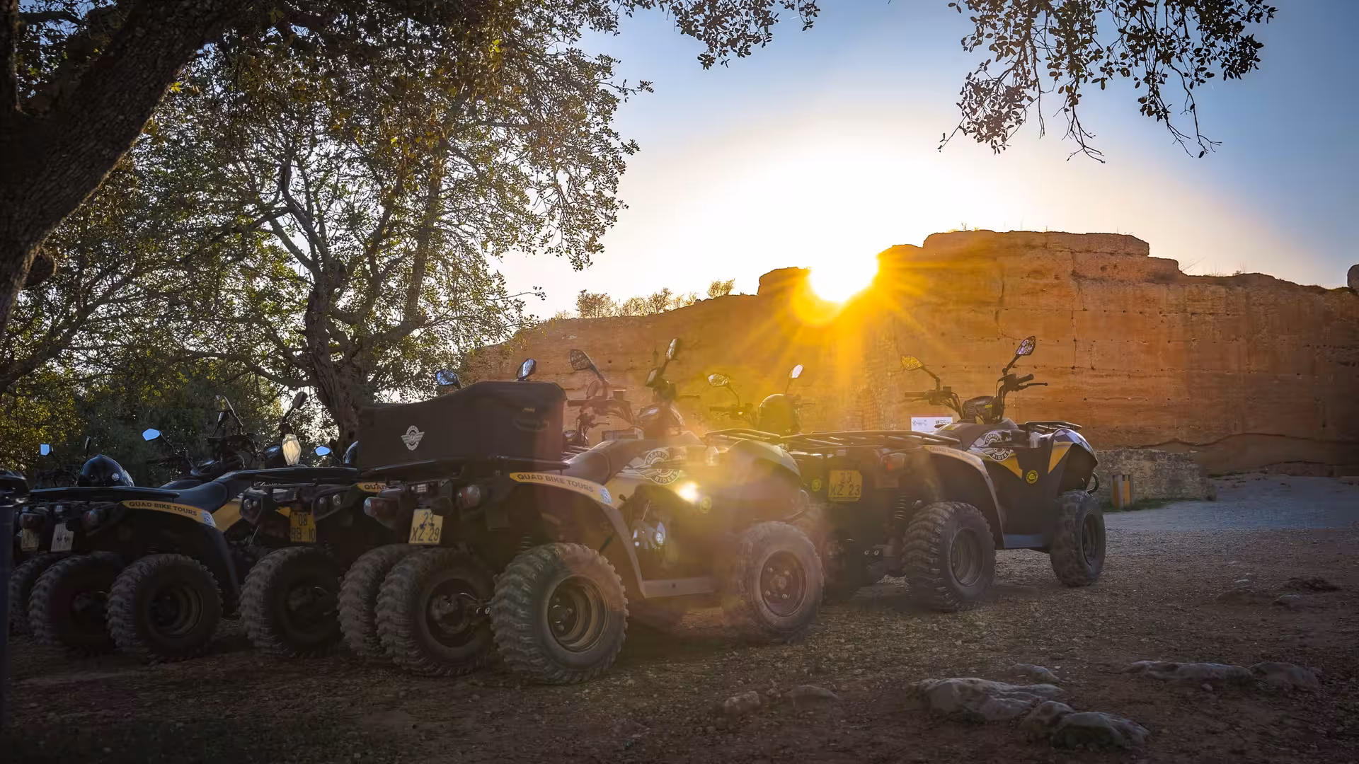 Parked quad bikes at sunset beside rugged cliffs and forest, ready for an off-road full day ATV adventure tour