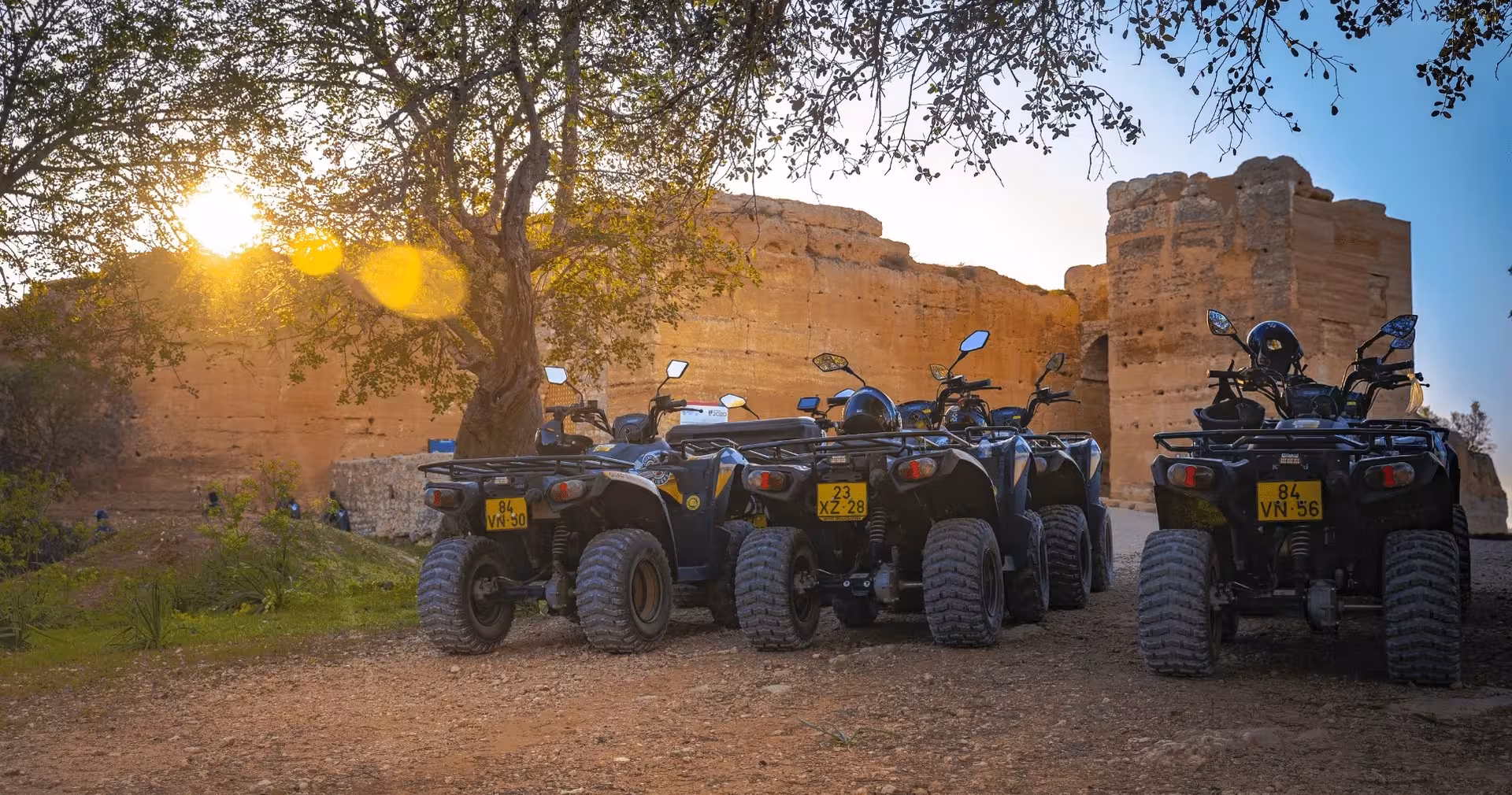 Row of parked quad bikes at sunset beside historic desert walls, ready for a guided half-day ATV adventure