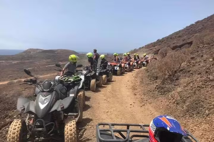 Group of quad bikers in helmets pause along a scenic trail overlooking expansive desert terrain.