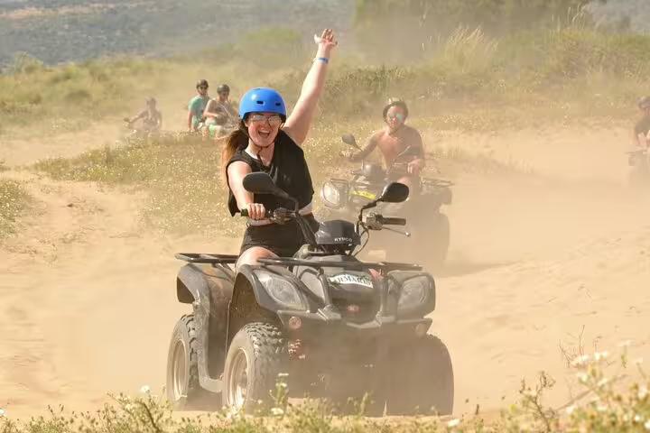 Excited rider raising an arm while leading a quad biking tour through dusty trails near Kusadasi Port.