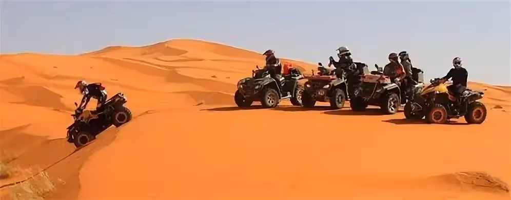 Group of quad riders navigating the majestic sand dunes of Merzouga Erg Chebbi Desert under a clear blue sky.