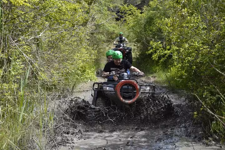 Riders on quad bikes splash through a muddy forest track on Antalya quad safari off-road adventure tour