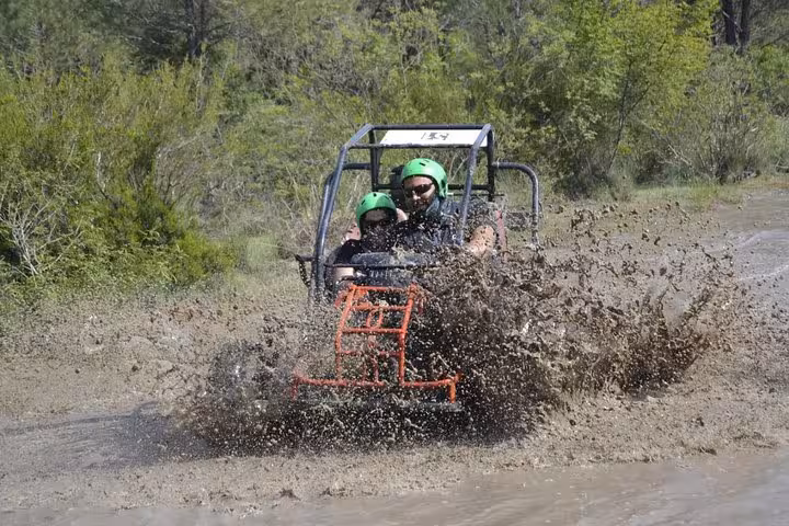 Riders in helmets splash through muddy water on Antalya quad safari adventure, off-road buggy thrill