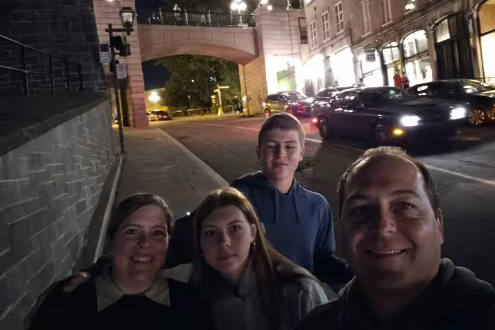 Family selfie at night near Old Quebec city gate and lit streets on Quebec City scavenger hunt walking tour