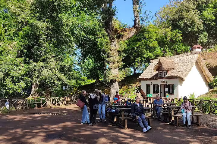 Visitors relax near a charming thatched-roof house at the Queimadas Natural Park, a starting point for the Caldeirão Verde hike.