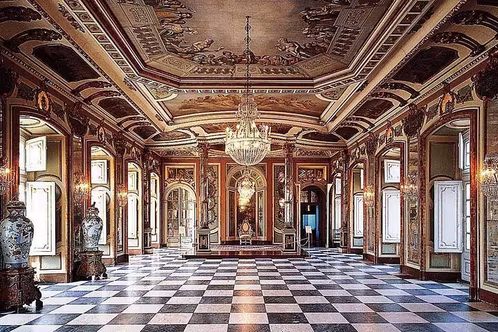 Opulent interior of Queluz Palace with intricate ceiling, chandeliers, and checkered floor, featured on Mafra, Ericeira tour.