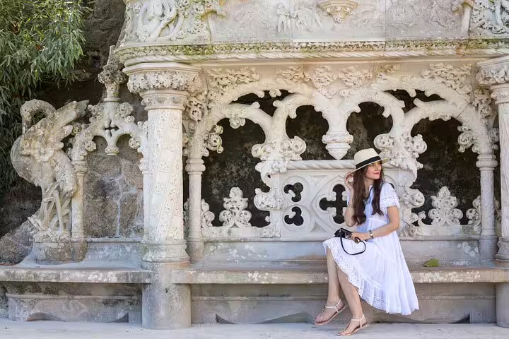 A woman in a white dress sits on an ornate stone bench at Quinta da Regaleira, Sintra during a private tour.