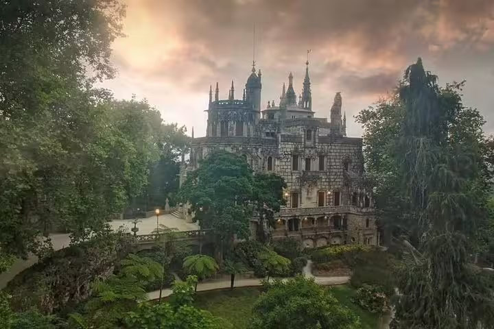 Majestic view of Quinta da Regaleira at sunset, surrounded by lush greenery, featured in Sintra's small-group full-day tour.