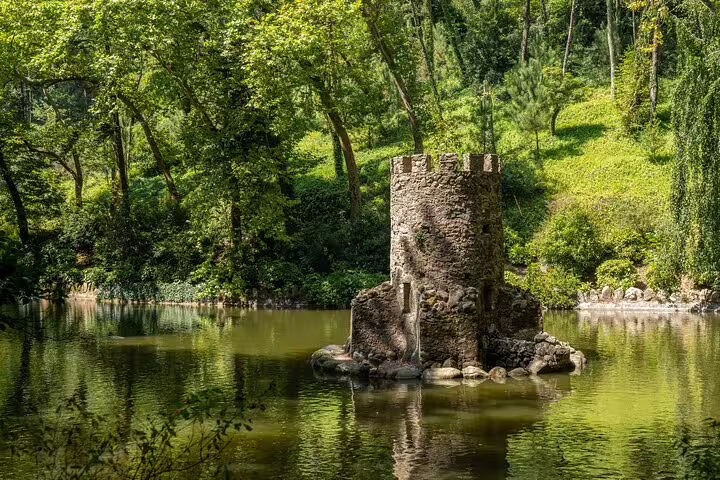 Medieval stone tower surrounded by lush greenery and tranquil water at Quinta da Regaleira in Sintra, Portugal.