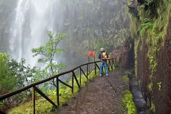 Hiker enjoys the breathtaking view of a powerful waterfall along the scenic trail at Rabaçal's 25 Fontes in Madeira.