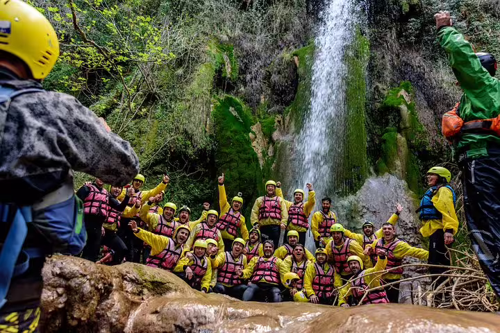 Group photo by lush waterfall after rafting Lousios and Alfeios rivers in Greece, wearing helmets and life vests
