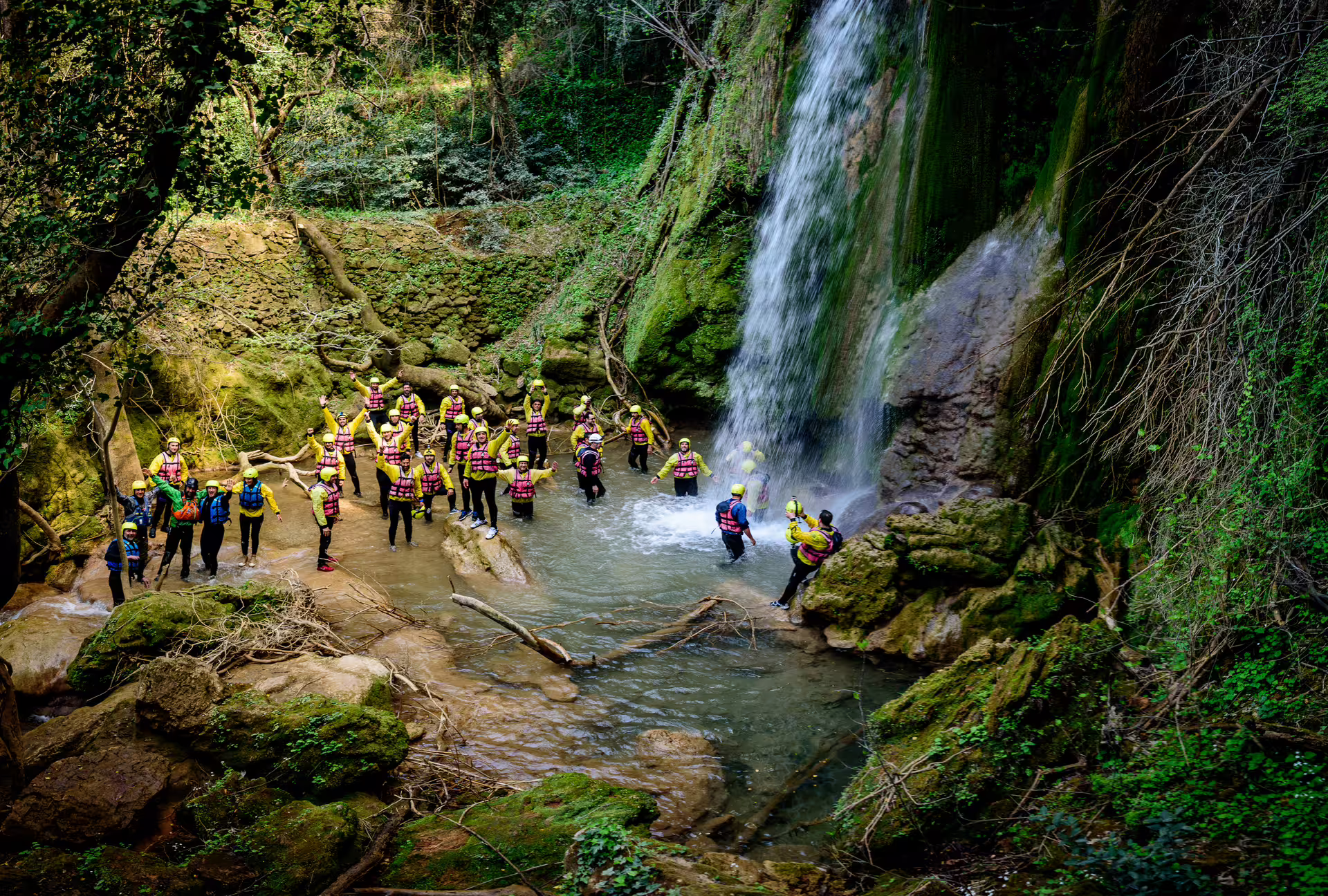 Rafting group in helmets and life jackets cooling off under a waterfall on the Lousios-Alfeios adventure tour