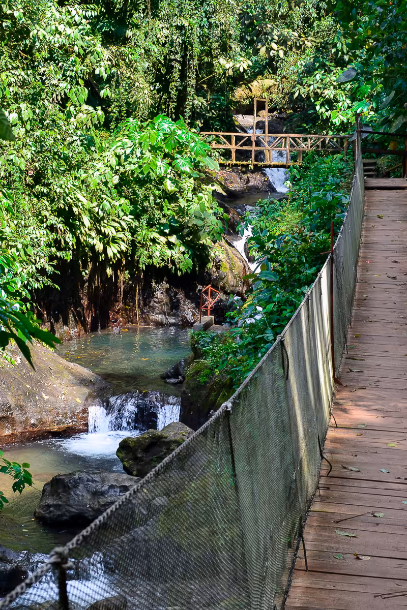 Scenic wooden bridge over a waterfall in the lush rainforest of Rainmaker Park, ideal for eco-tourism from Manuel Antonio.