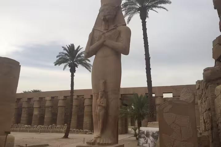 Colossal Ramses II statue at Luxor Temple with palm trees, private day trip to Luxor from Hurghada