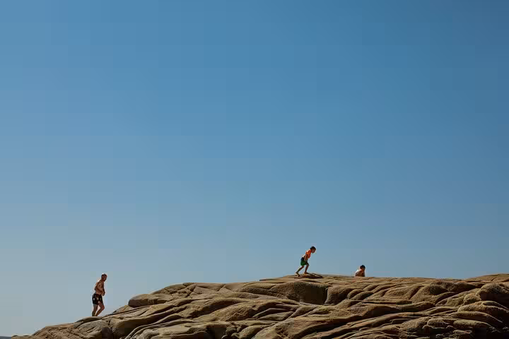 Hikers exploring sunlit rock formations above Seychelles Beach on Ikaria during Randi Forest coastal hike and boat excursion
