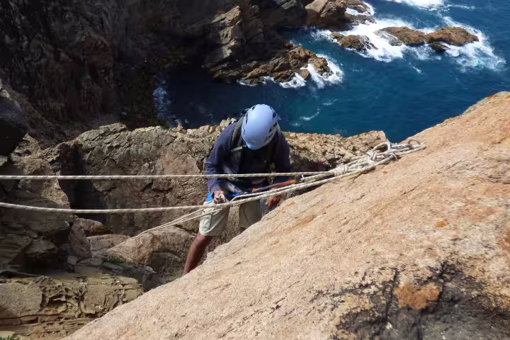 Adventurer rappelling down a rugged cliff with ocean views on an exhilarating Sintra circuit tour, perfect for thrill-seekers.