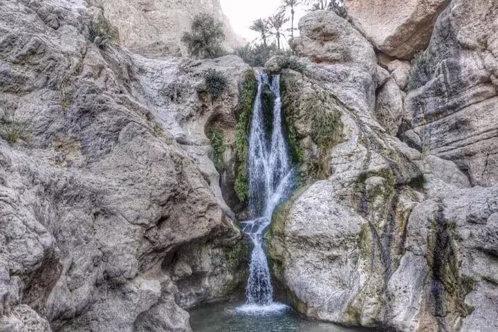 Discover a serene waterfall cascading into a tranquil pool amidst rocky terrain on the Ras Al Hadd camping tour.