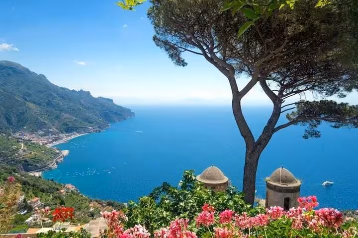 Scenic view of Ravello's coastline with lush greenery and vibrant flowers overlooking the Amalfi Coast's blue waters.