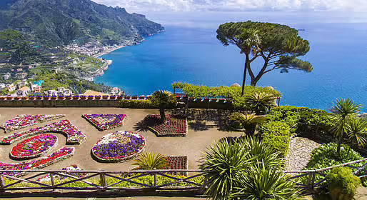 Panoramic view from Ravello gardens overlooking the Amalfi Coast cliffs, terraced flowers and turquoise Tyrrhenian Sea.