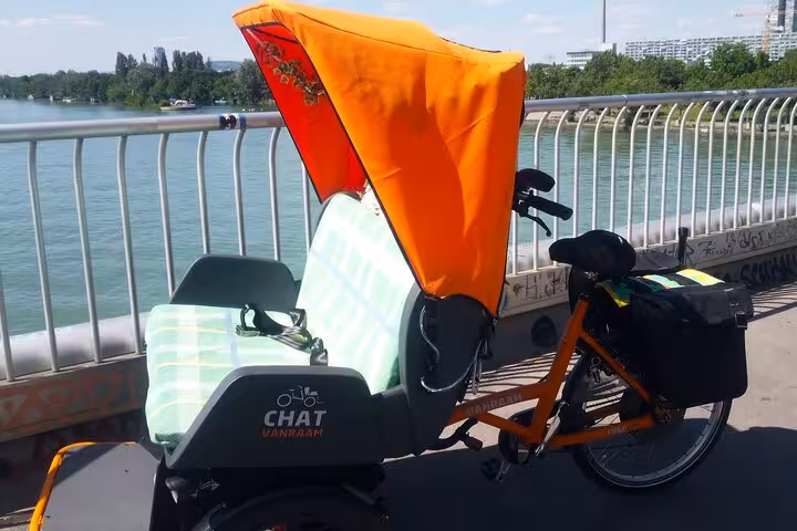RAXI e-rickshaw with orange canopy on Danube riverside, scenic big private Vienna tour by e-rickshaw