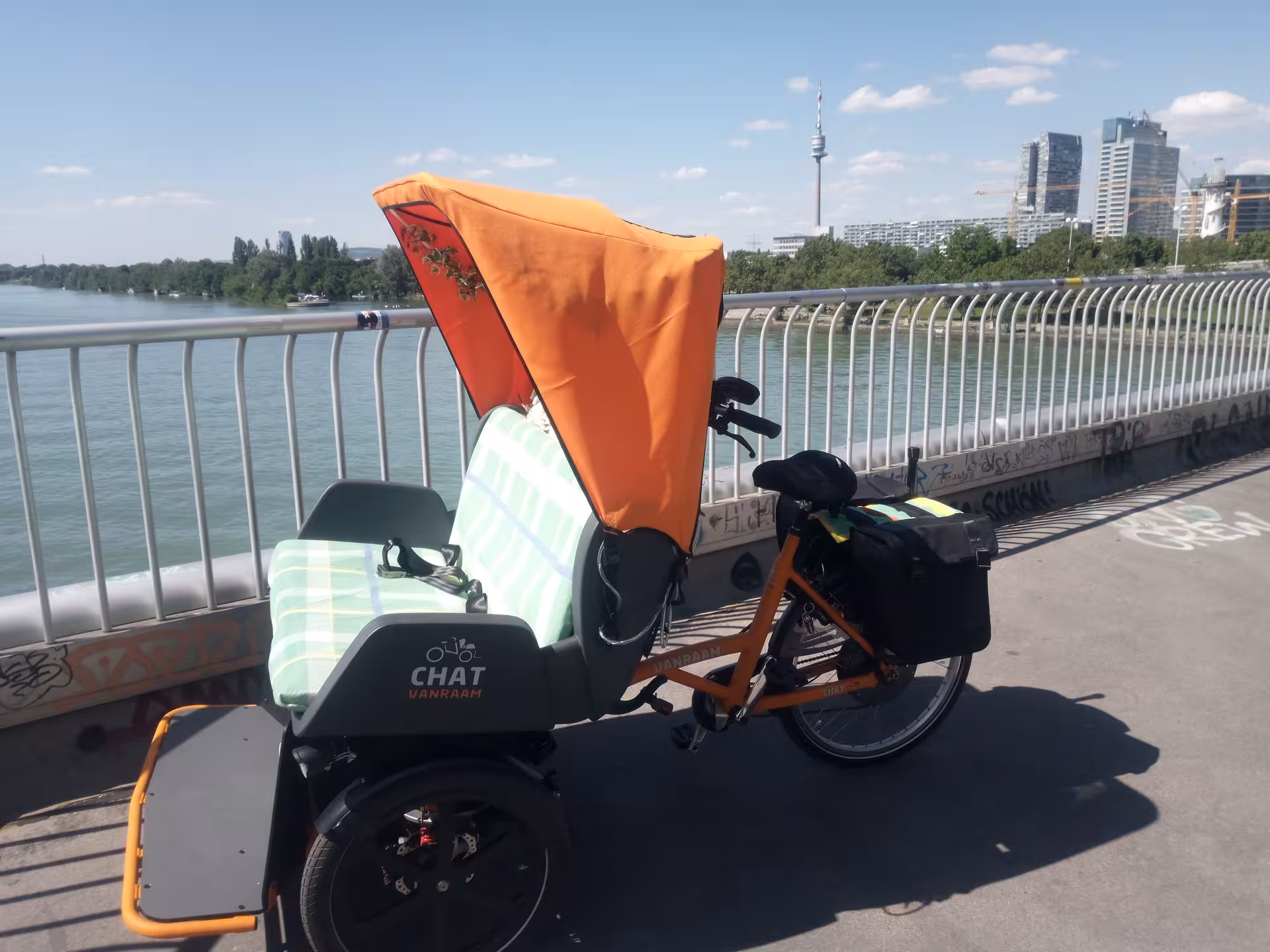 Electric rickshaw RAXI by the Danube with Vienna skyline and Danube Tower, panoramic eco-friendly tour ride