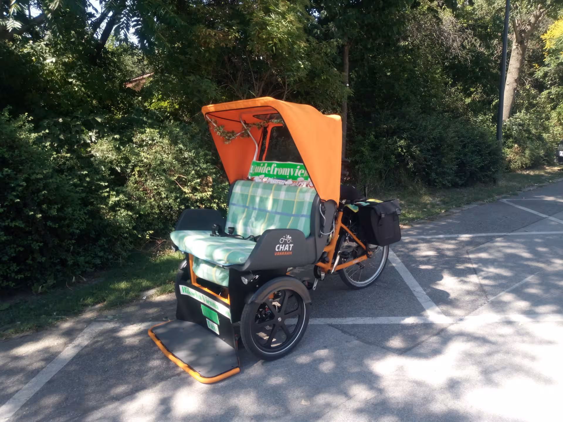 Orange-canopy RAXI electric rickshaw on Vienna cycle path, quiet panoramic city tour transport