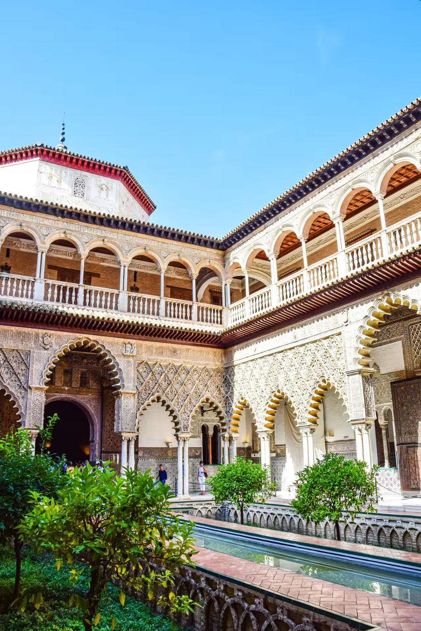 Sunlit courtyard of the Real Alcázar of Seville featuring lush greenery and exquisite Mudejar archways.