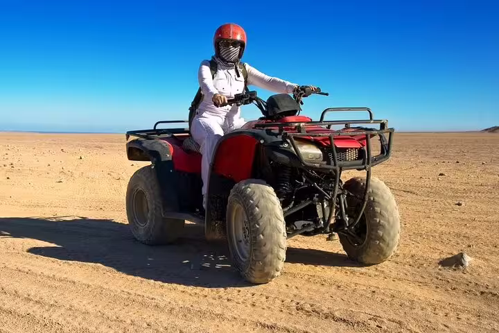 Helmeted rider on red ATV quad bike in open Sinai desert near Sharm El Sheikh on guided safari adventure tour