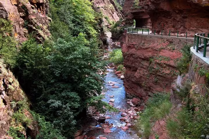 Picturesque canyon trail alongside a flowing stream with lush vegetation and vibrant red rock walls in Red Canyon.