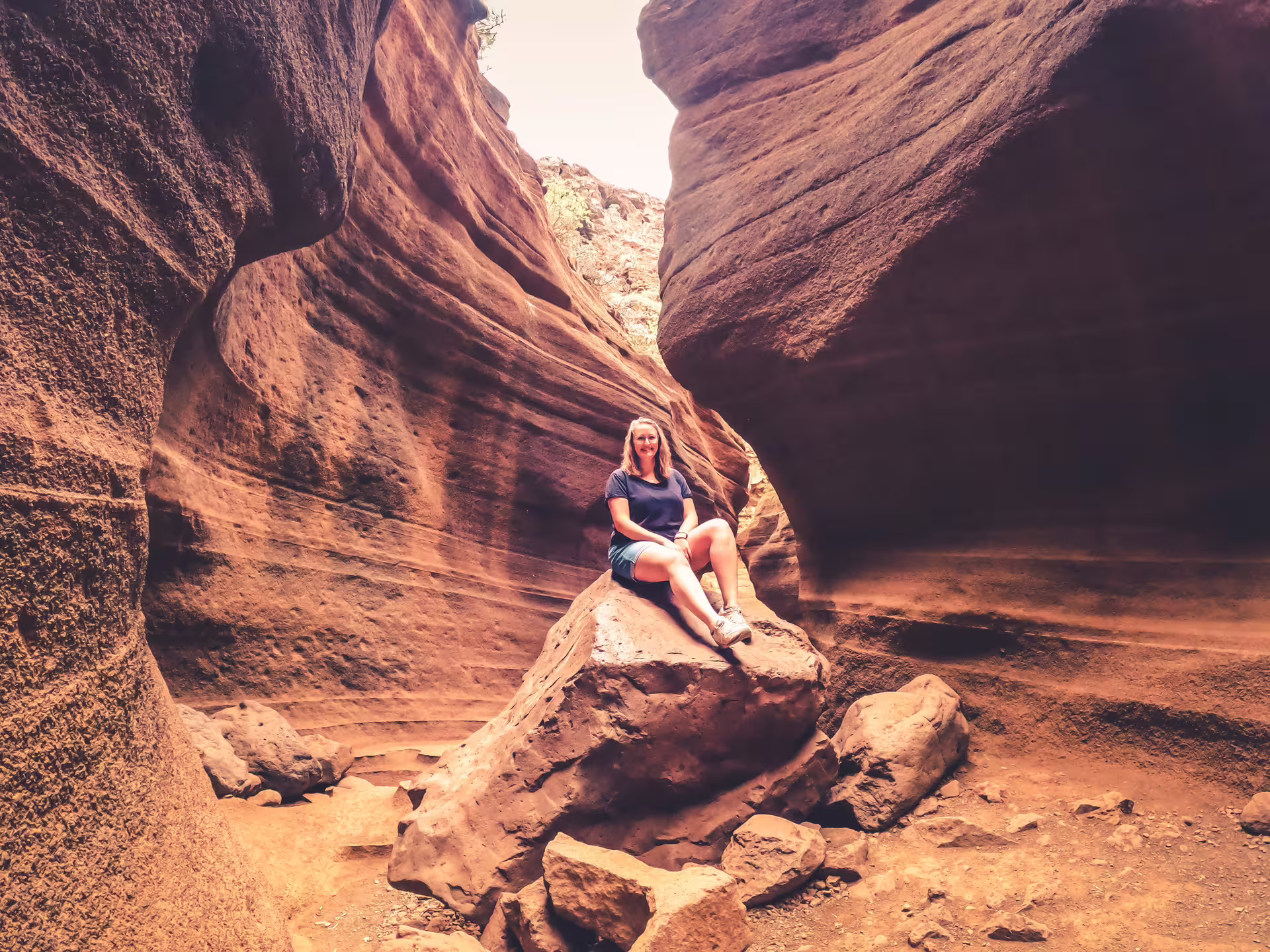 Visitor sitting on a rock in the stunning Red Canyon, showcasing the unique geological formations of the tour.