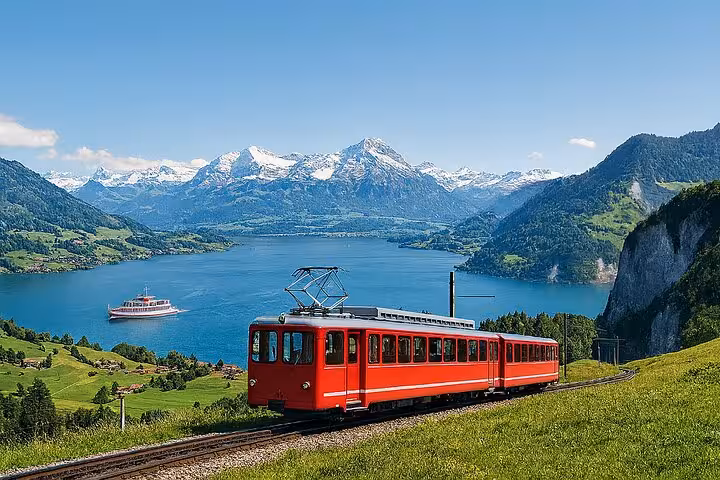 Red cogwheel train traveling beside a lake with stunning views of the snow-capped Swiss Alps.