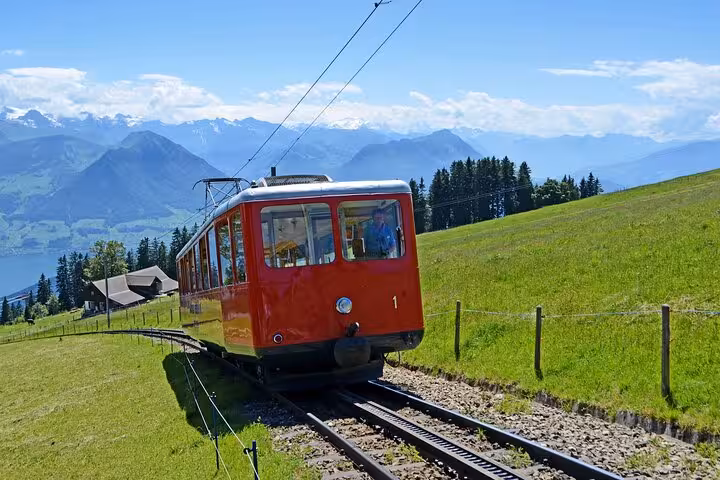 Red cogwheel train traversing lush Swiss Alps with panoramic mountain and lake views.