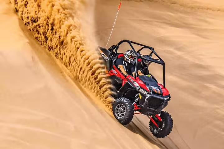Adventurous ride down a steep sand dune in Dubai on a powerful red dune buggy, kicking up golden sand.