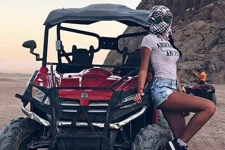 Woman posing by red dune buggy on Sharm El Sheikh desert safari, family buggy adventure with canyon views