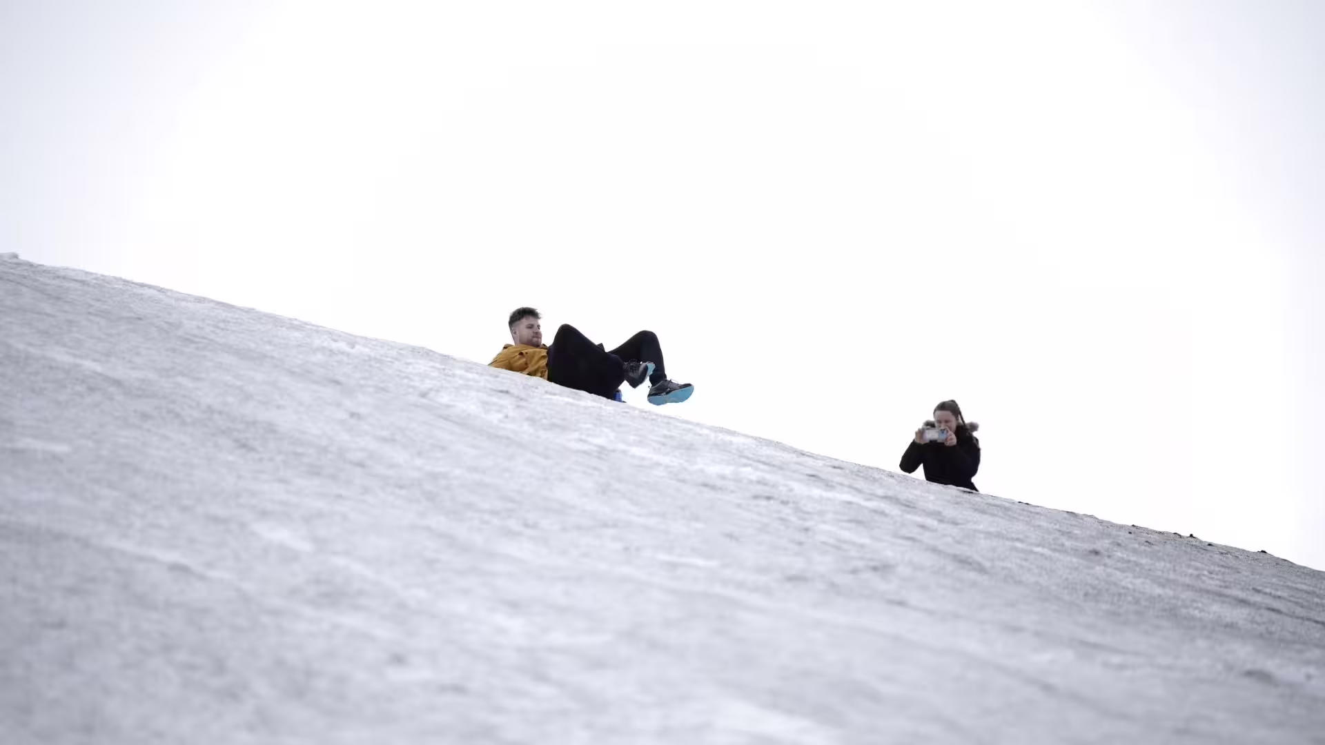 Traveler sledding down a snowy slope on Langjökull Glacier, Iceland, on Red Glacier monster truck tour from Gullfoss