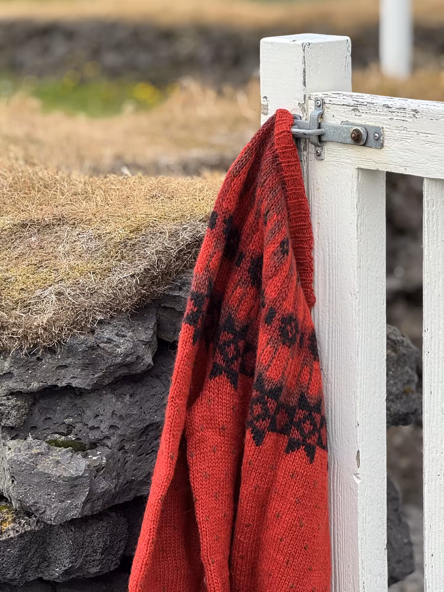 Red Icelandic wool sweater with traditional patterns hanging on a wooden gate, ideal for the Iceland Winter Knitting Tour.