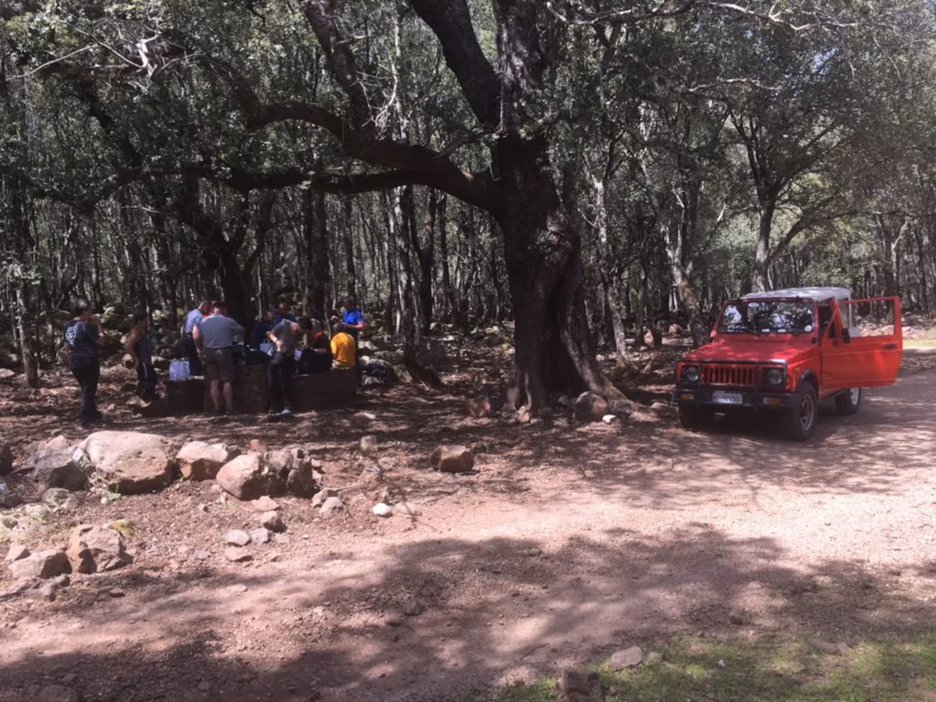 A red Jeep parked in a forested area with a group enjoying a break on a Supramonte tour from Cala Gonone.