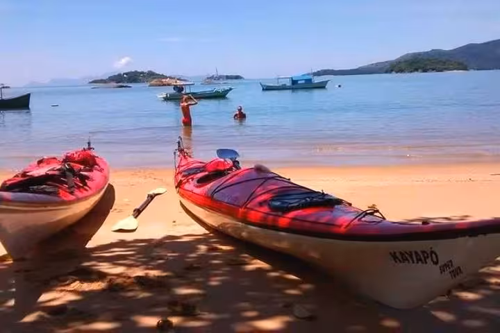 Two red kayaks on a sandy beach overlooking a serene bay, part of the Mangrove and Beach Kayak Tour by Paraty Tours.