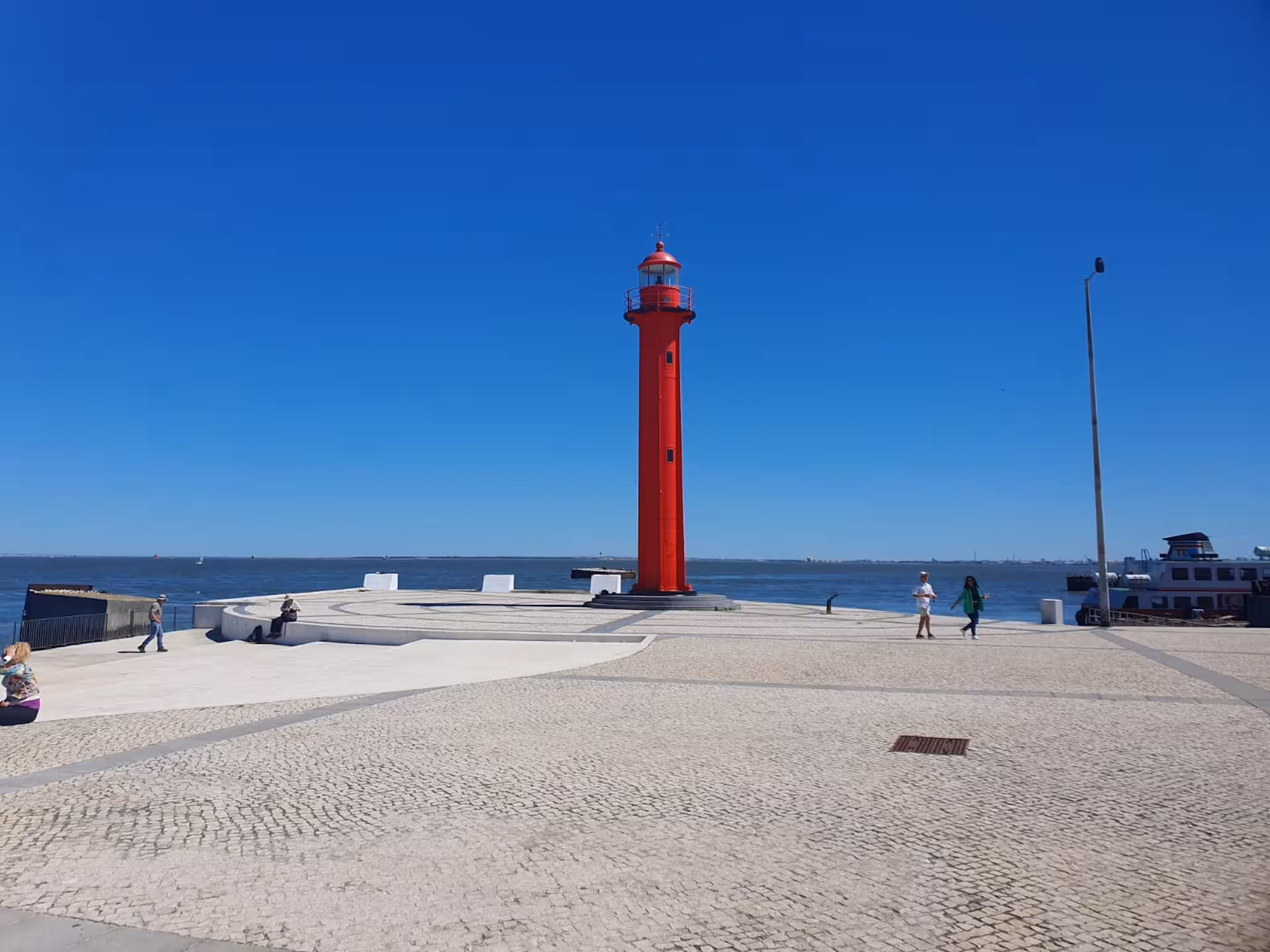 Red lighthouse on Almada's waterfront under a clear blue sky, highlighting Lisbon's maritime charm.